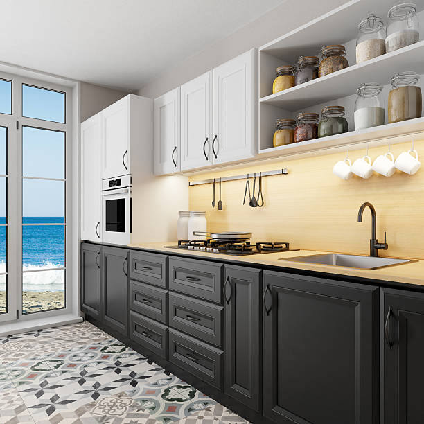 Interior view of a modern Scandinavian-style kitchen with clean lines, light wood surfaces, and a minimalist layout. The space features white upper cabinets, dark lower units, a soft yellow backsplash, and a compact dining area with black chairs and pendant lighting. Ideal for visuals focused on simple living, Nordic design, home organization, and contemporary lifestyle.