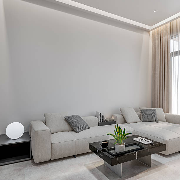 Modern living room interior with a large empty wall above a light-colored sectional sofa, designed in a clean, minimalist style. Neutral tones, soft natural light, and contemporary furniture create a calm, elegant atmosphere with generous copy space, ideal for interior design, lifestyle, or real estate concepts. 3D rendered image.